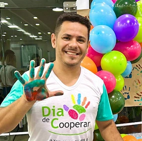  homem branco, moreno com camisa branca com verde e mão pintada com tintas de diversas cores 