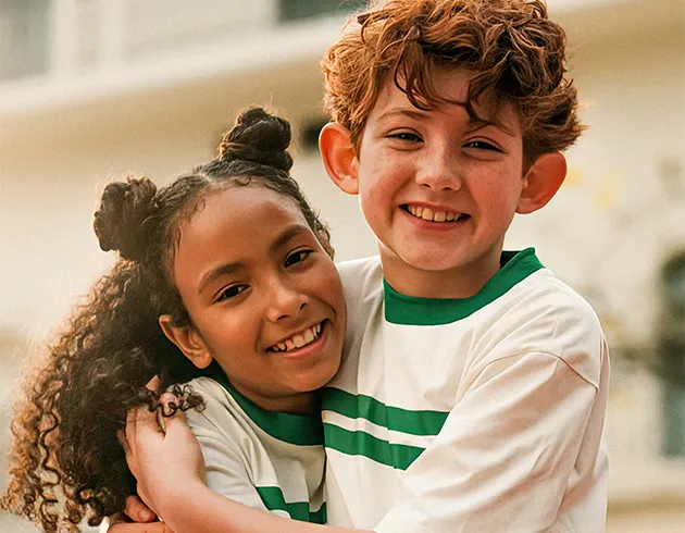  A imagem apresenta duas crianças com sorriso no rosto e se abraçando 